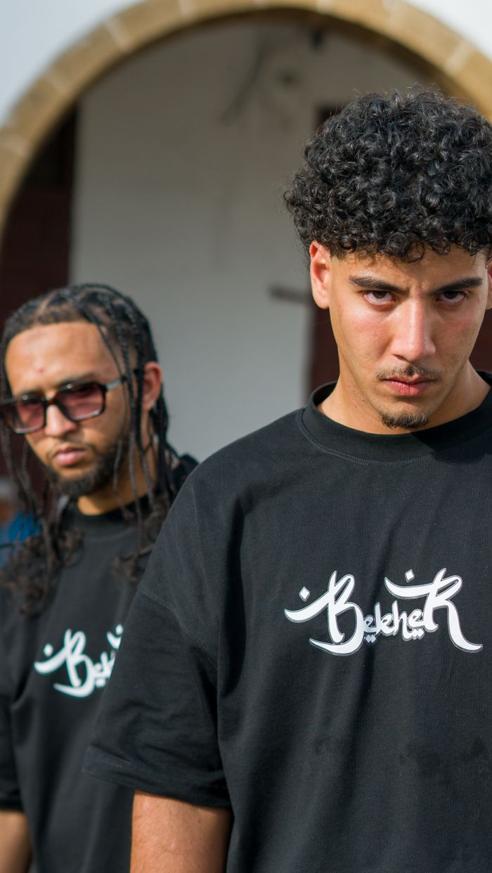 Mastering the First Impression: Your intriguing post title goes here Two young men pose wearing black t-shirts with logo design, outdoors in Morocco.