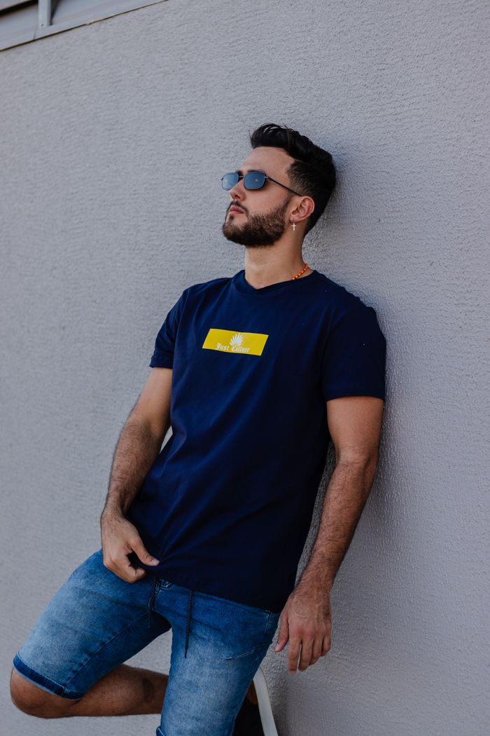 team-03 Fashionable man in denim shorts and sunglasses leaning against a wall outdoors.