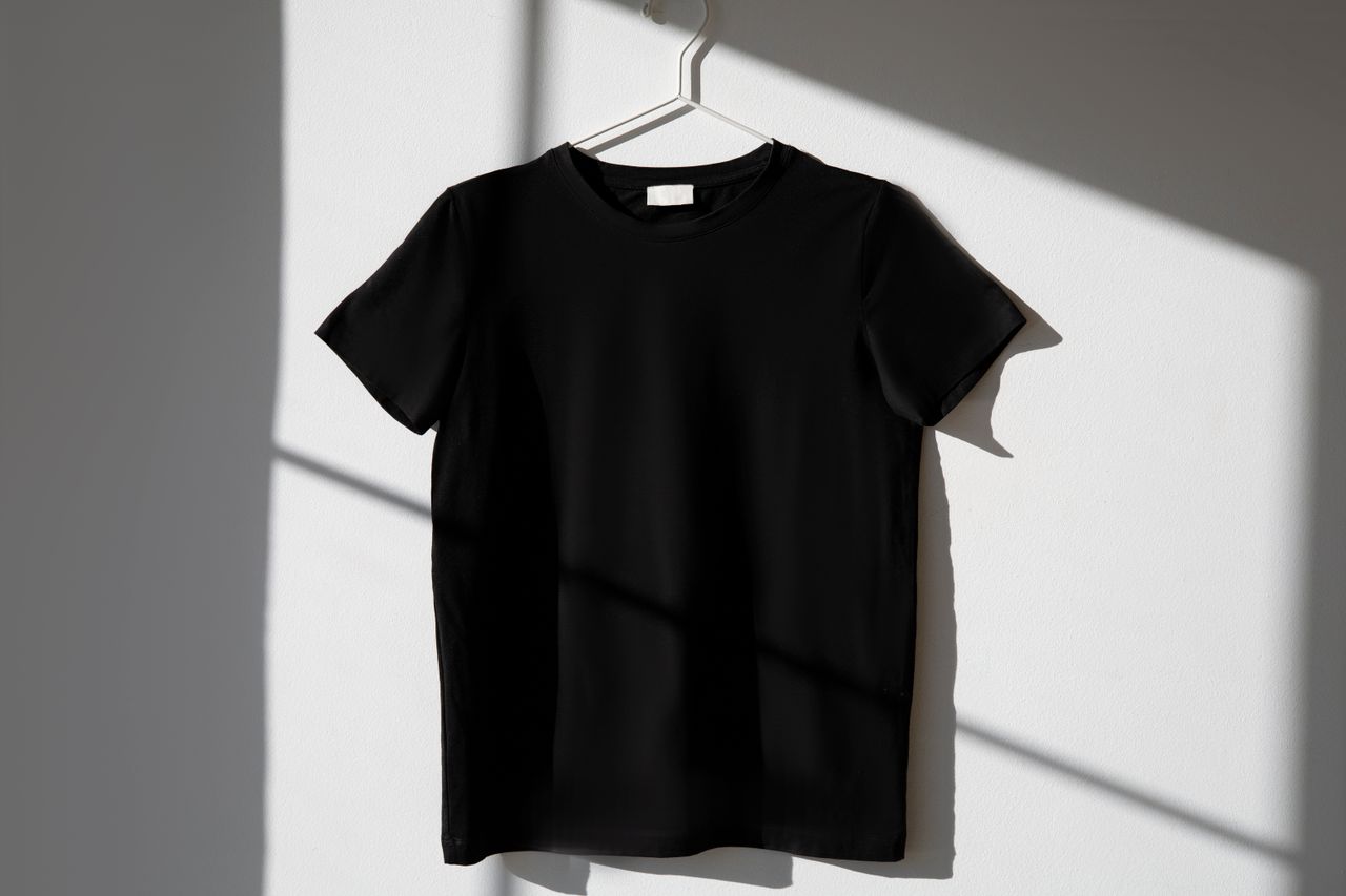 team-02 Minimalist image of a black t-shirt on a hanger with dramatic shadows on a white wall.